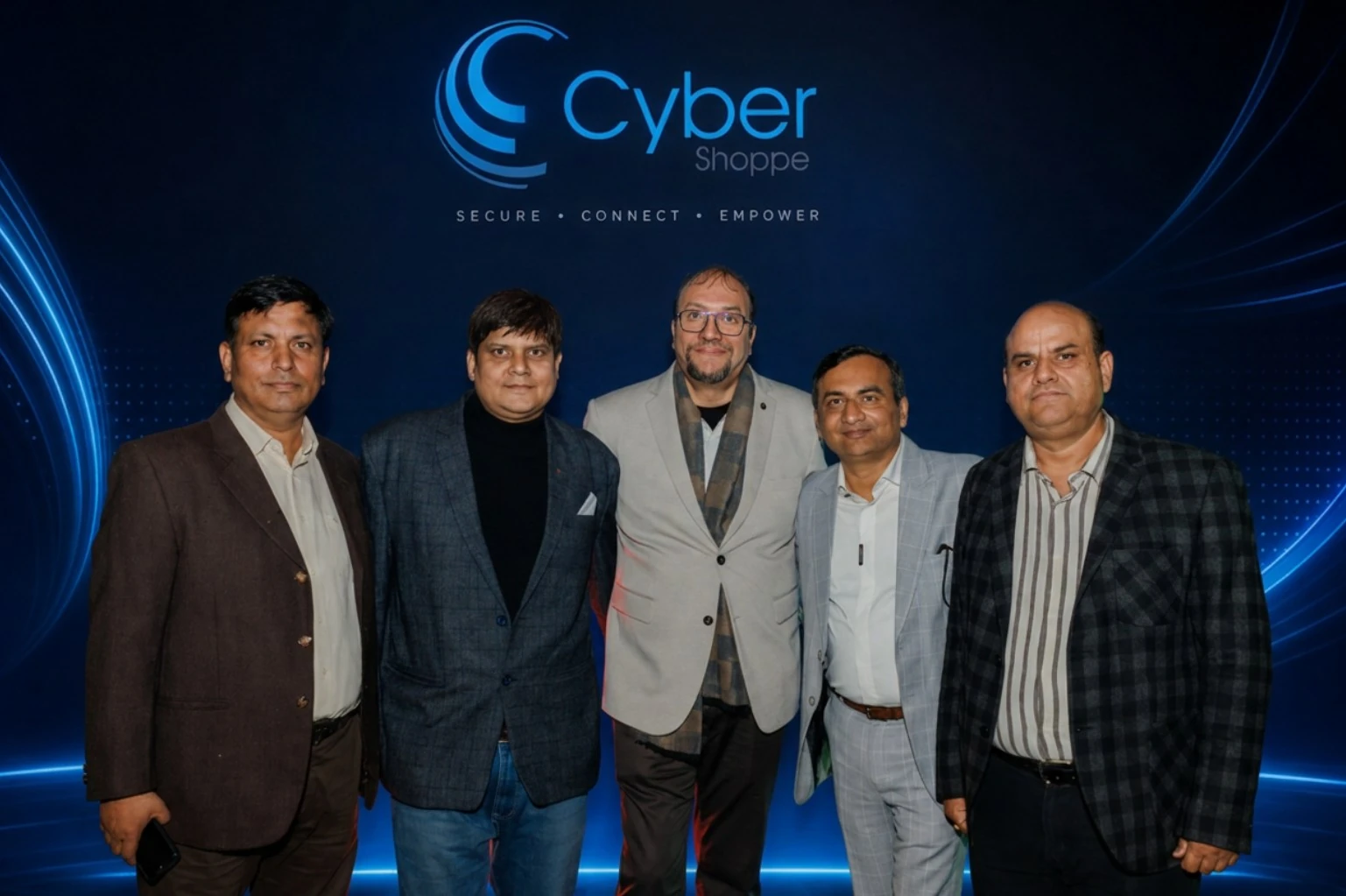 Five members of the Cyber Shoppe team standing together in front of a lit branded backdrop reading Cyber Shoppe, Secure · Connect · Empower.